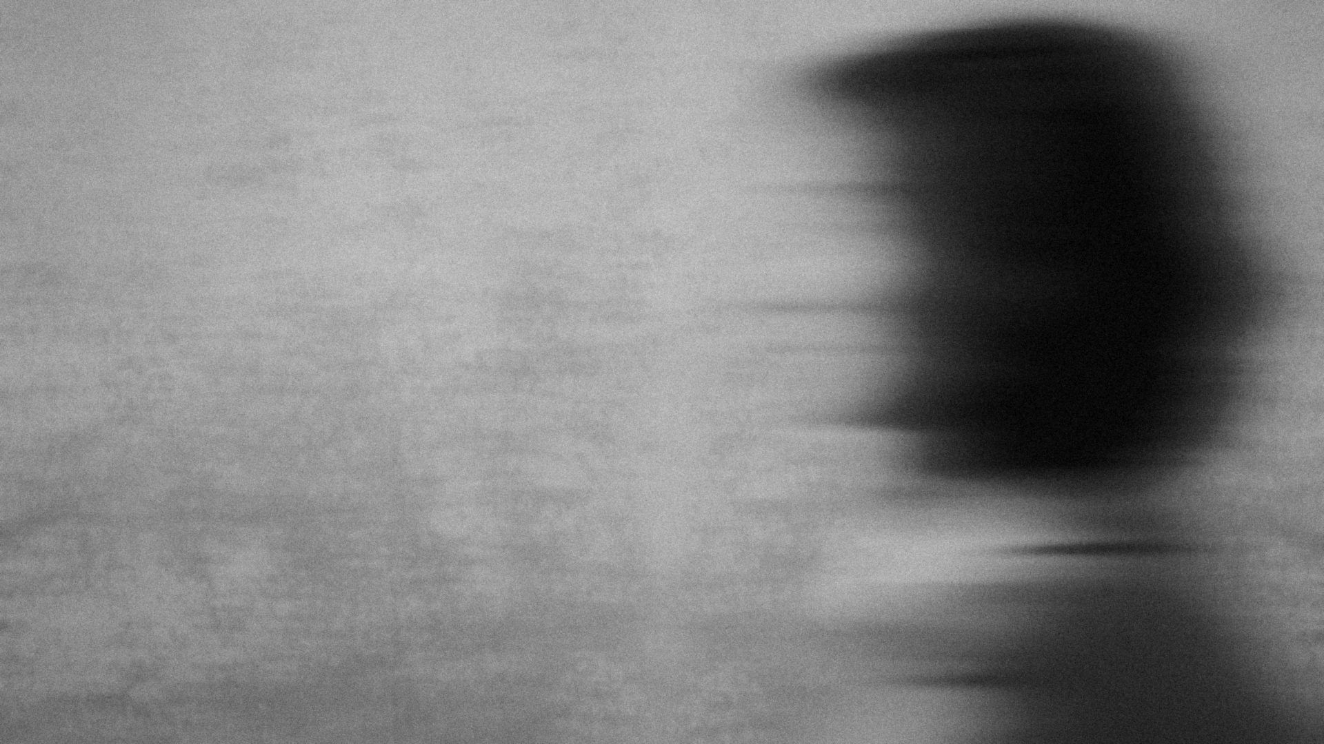 A motion-blurred figure walking past a grey wall