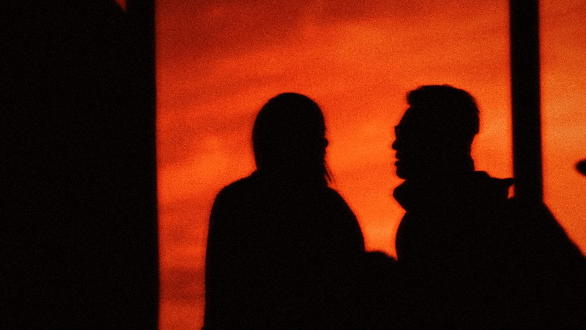 Two people in conversation against a red sky