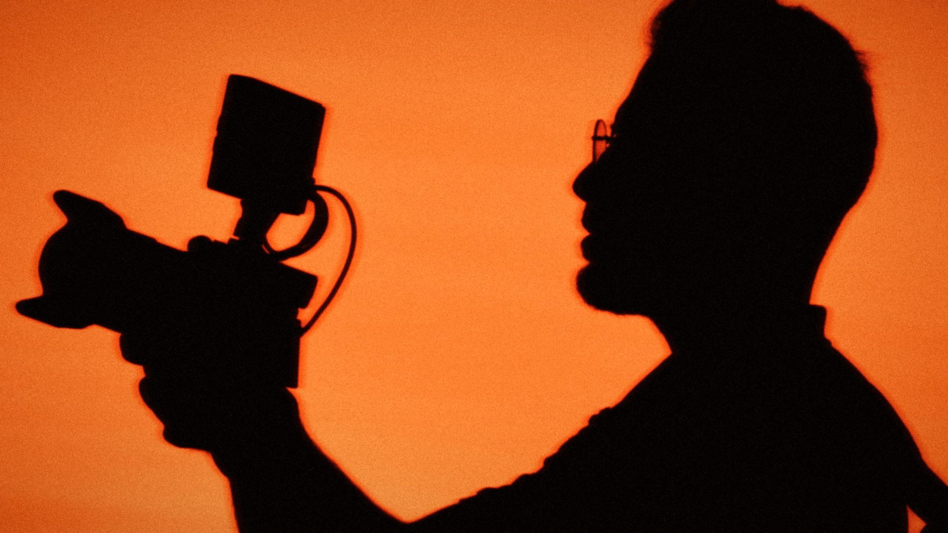 A videographer filming against an orange sky